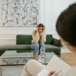 A woman looks distressed during a therapy session indoors, emphasizing mental health support.